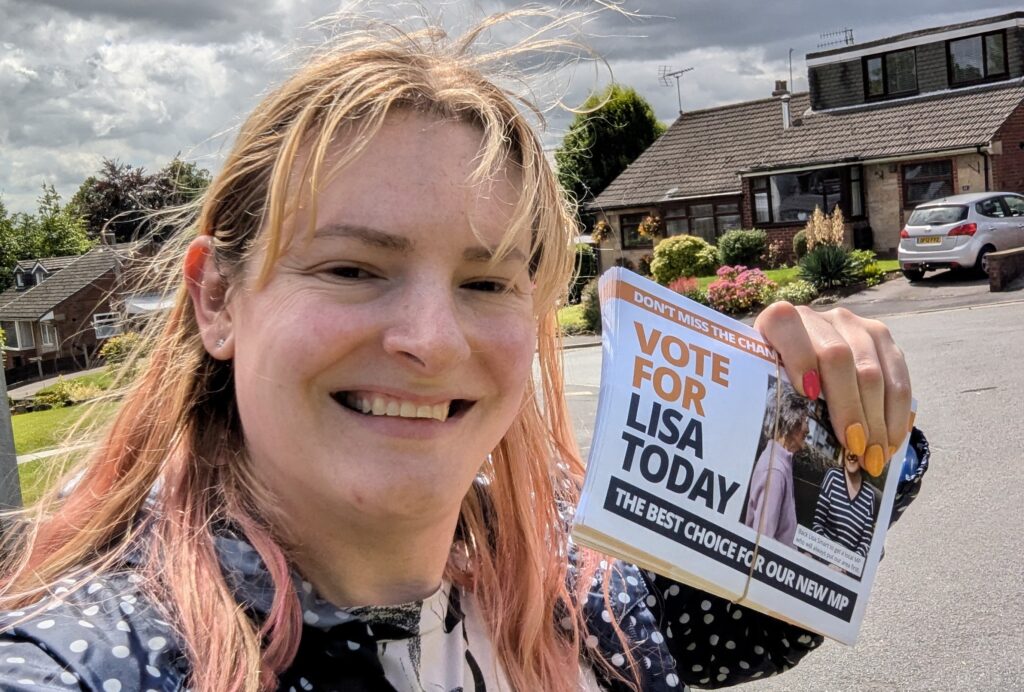 Chris Northwood smiles in a street on election day holding leaflets saying "Vote for Lisa Today, the best choice for our new MP".